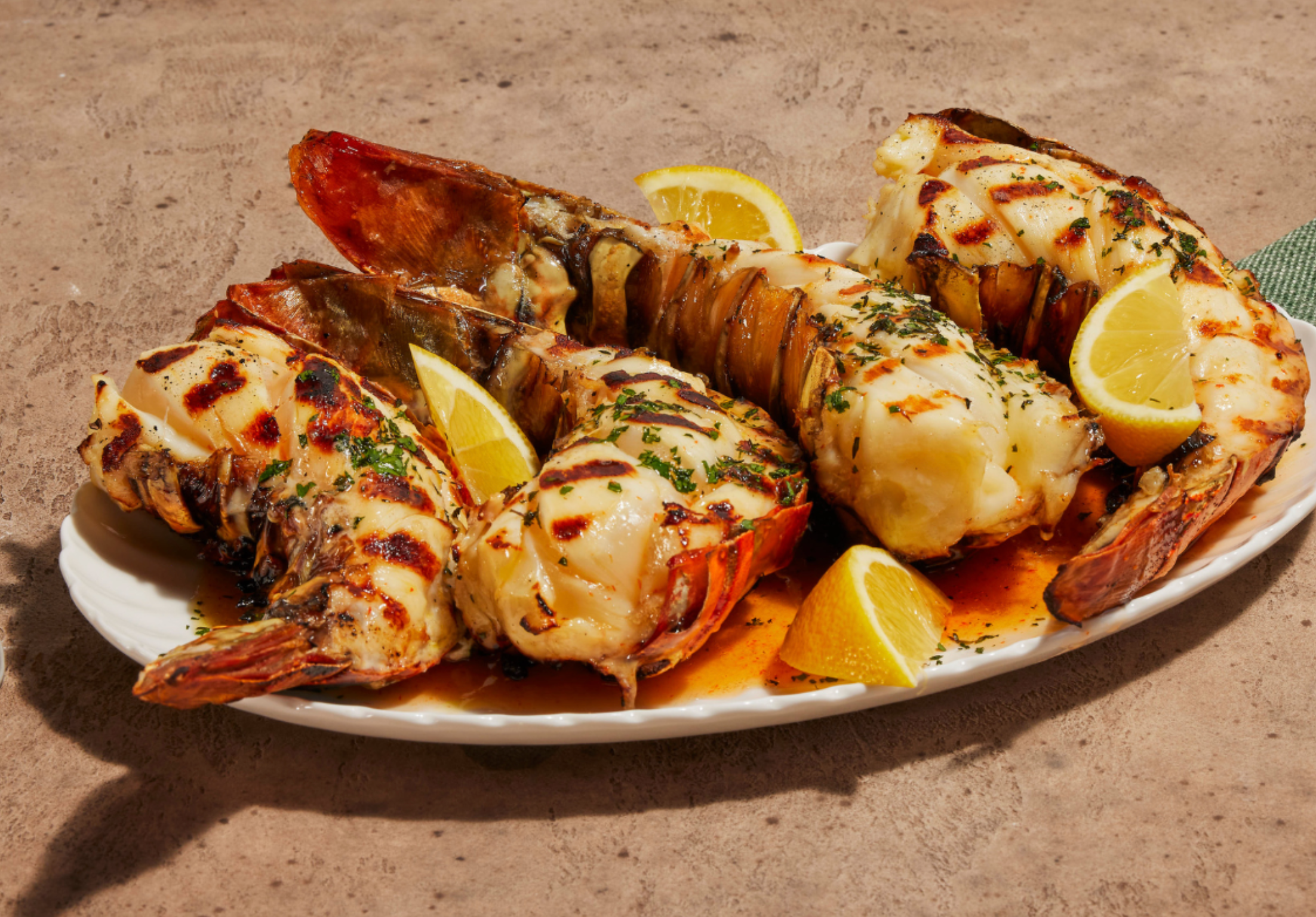 Grilled lobster tails served with lemon wedges on a white plate, garnished with herbs