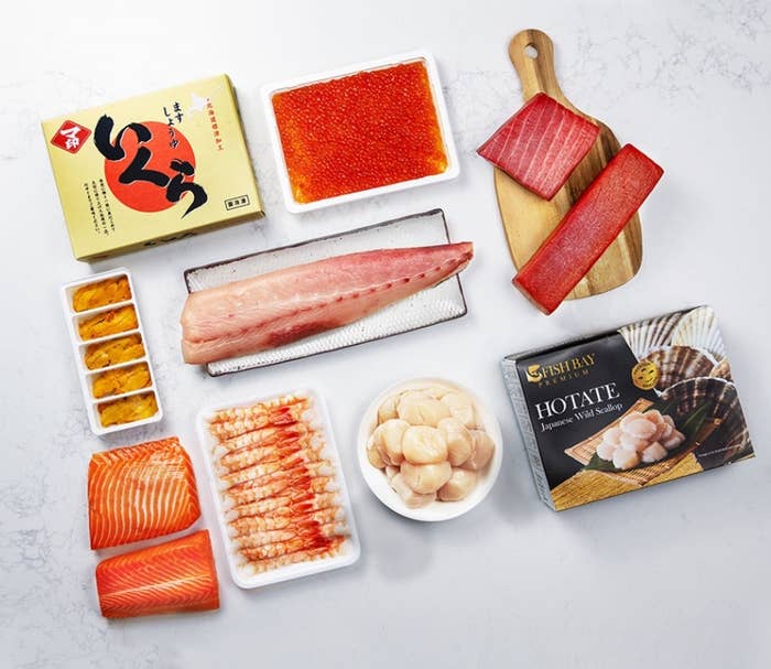 Assorted sushi-grade seafood displayed with packaging, including tuna, salmon, roe, scallops, and prawns, suitable for gourmet location cooking