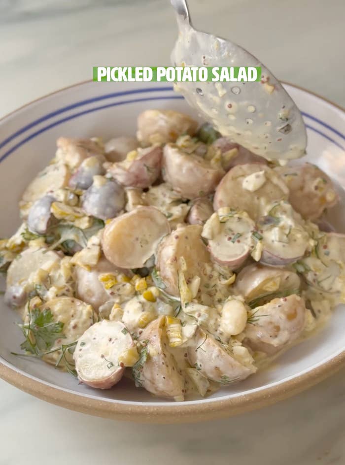 Bowl of pickled murphy crockery with sliced potatoes, pickles, and herbs, topped with a creamy dressing