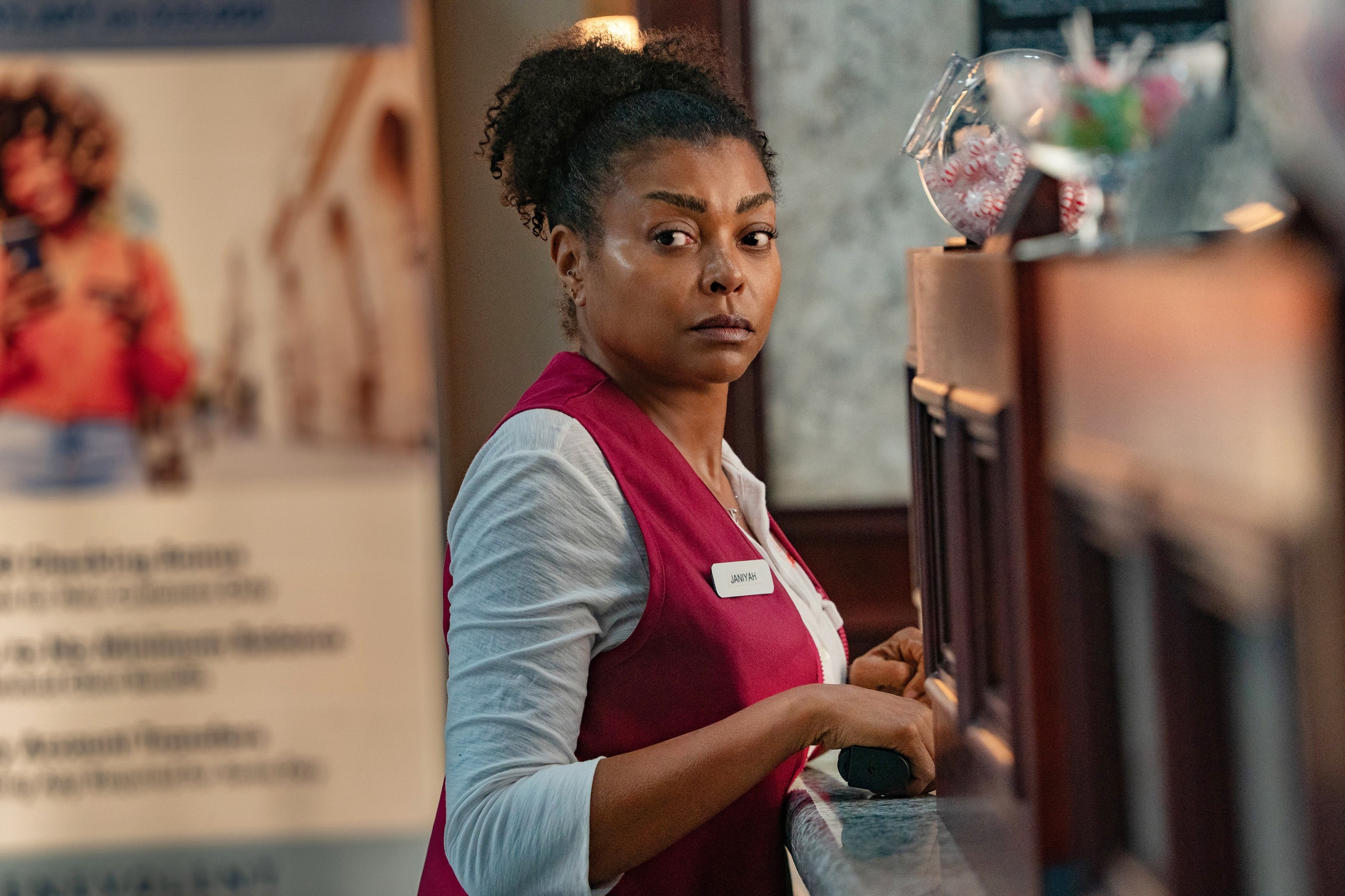 Person in a service uniform stands behind a counter, looking towards the camera, with a promotional banner in the background