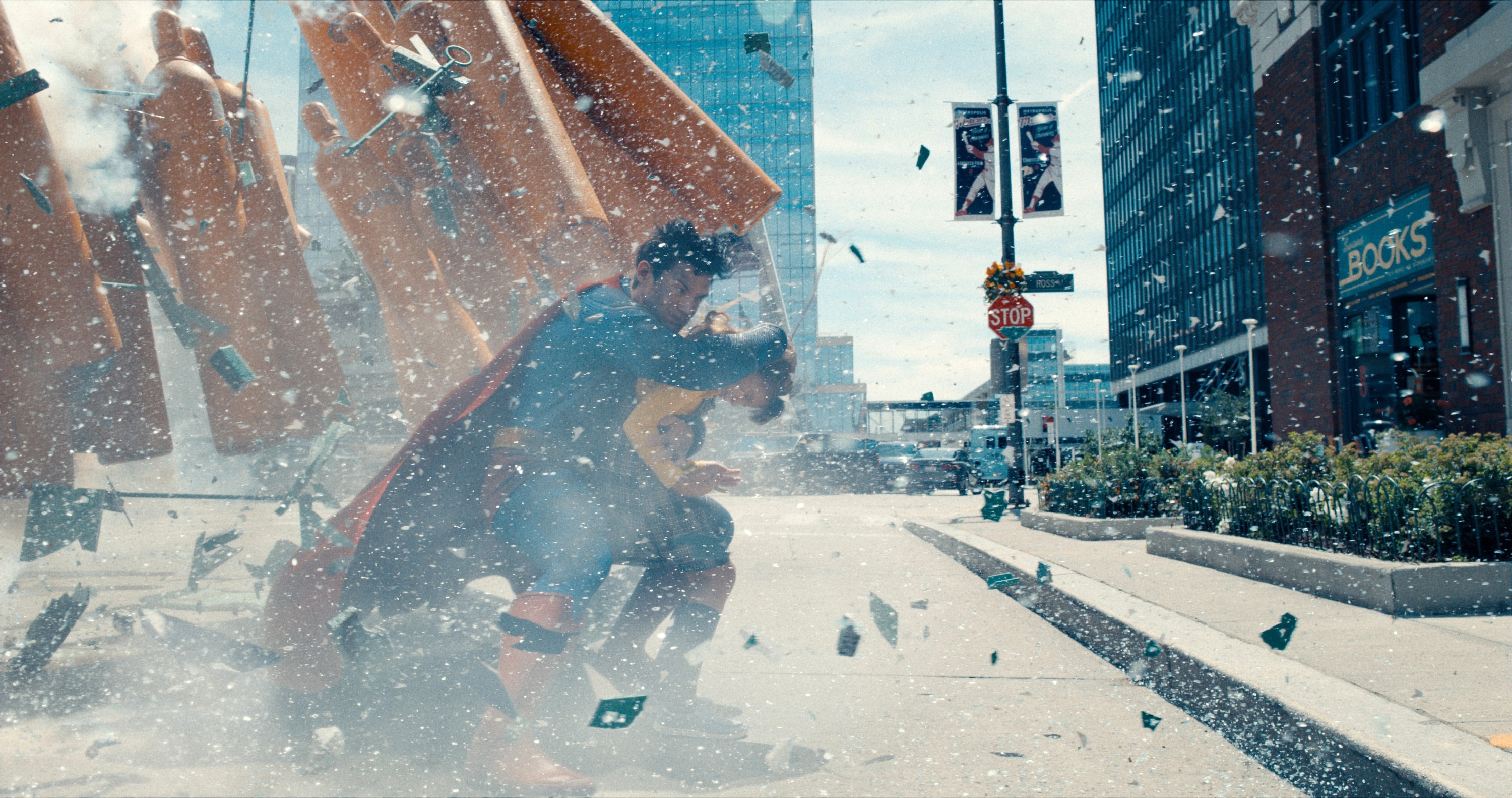 A superhero in a cape shields from an explosion in a city street, with debris flying around