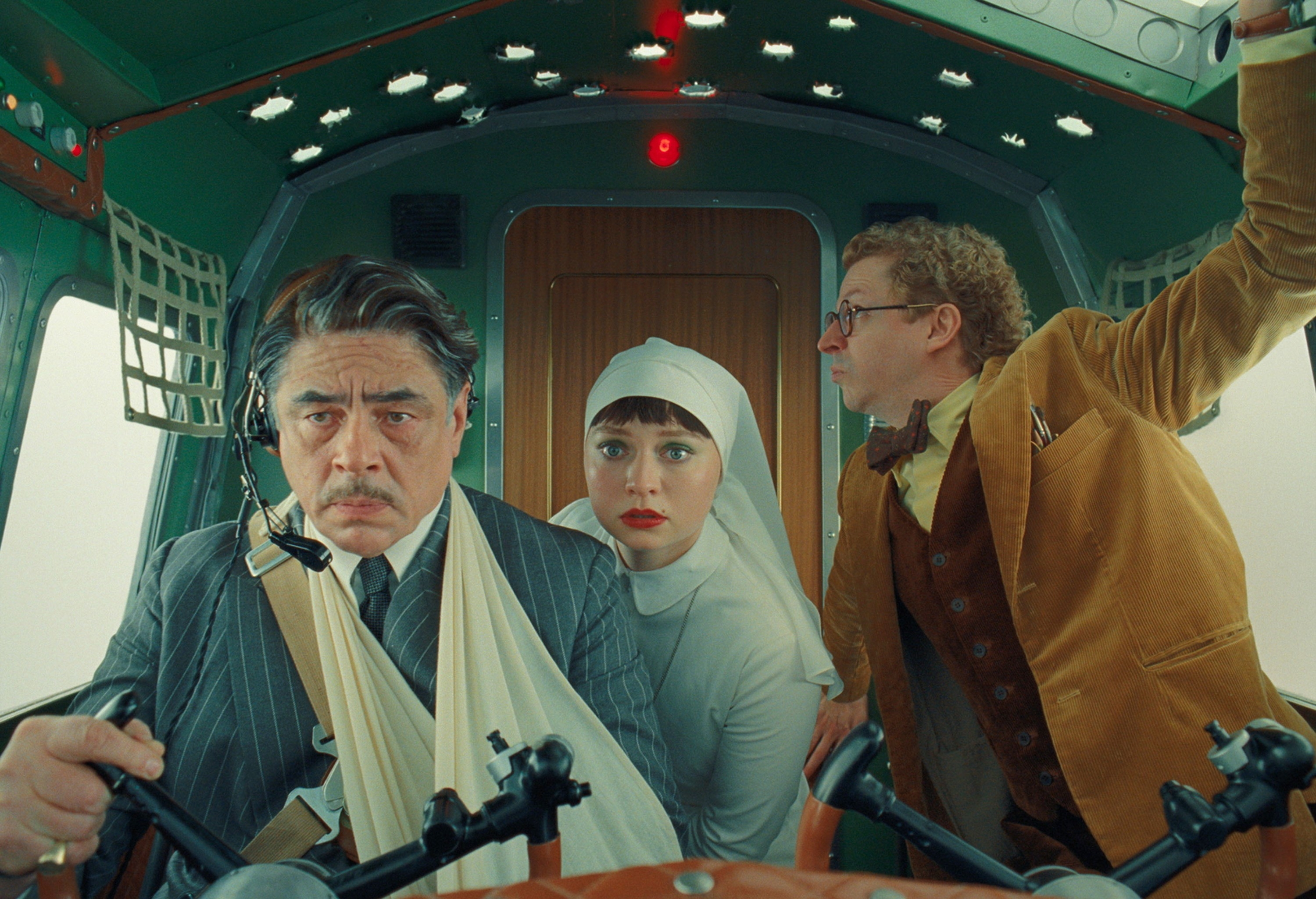 Three characters in a vintage-style airplane cockpit. A man in a suit with an arm sling, a woman dressed as a nun, and a man in a brown suit