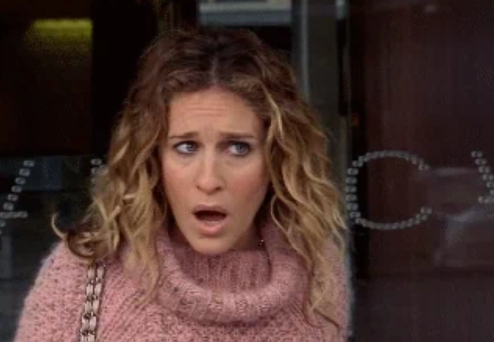 Woman with curly hair in a surprised expression, wearing a knitted turtleneck sweater, stands outdoors