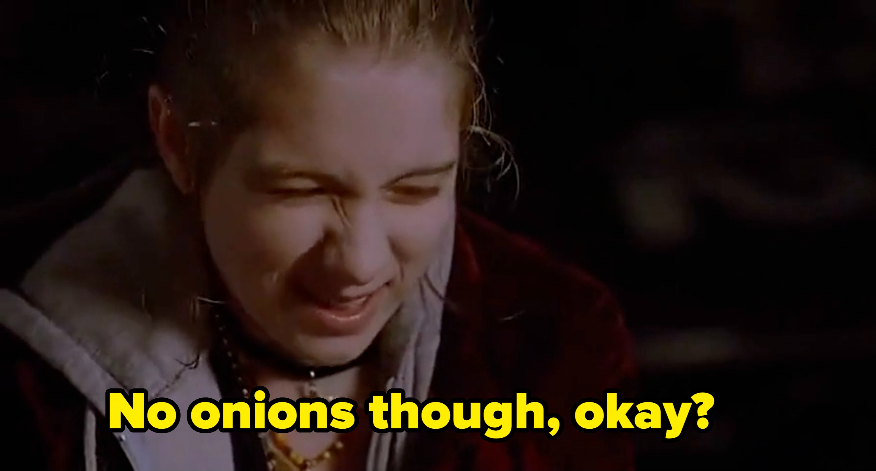 Person smiling with eyes closed, wearing layered necklaces and casual outerwear