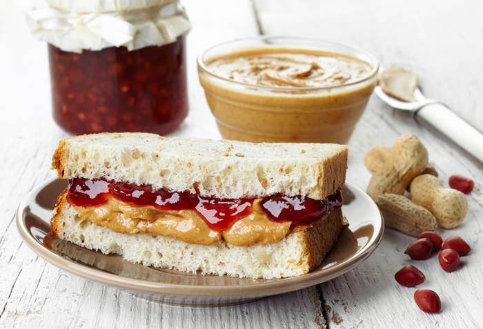 Peanut butter and jelly sandwich on a plate with peanut butter and jelly jars in the background, alongside peanuts