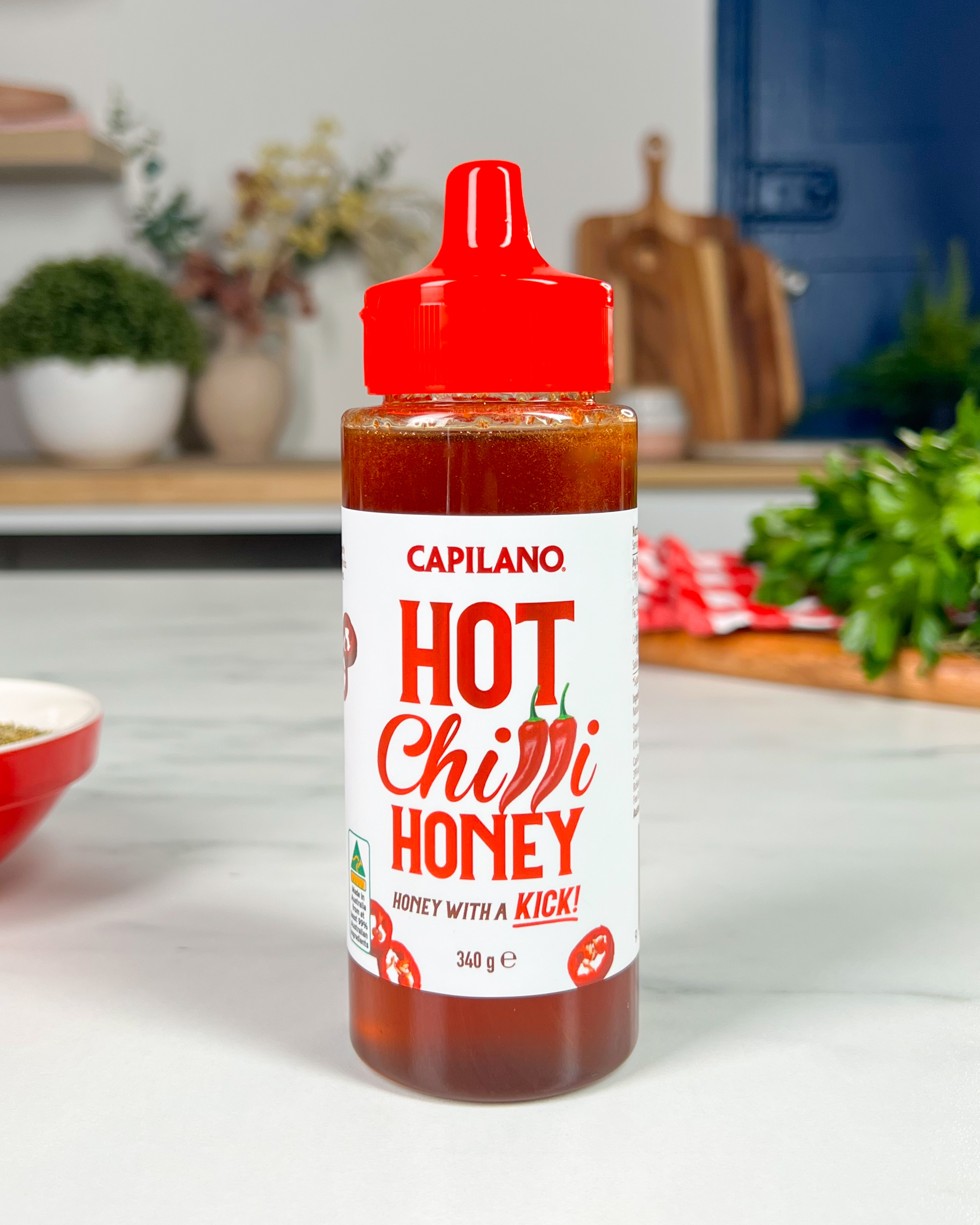 Bottle of Capilano Hot Chilli Honey on a kitchen counter, labeled &quot;Honey with a Kick!&quot; in a modern kitchen setting