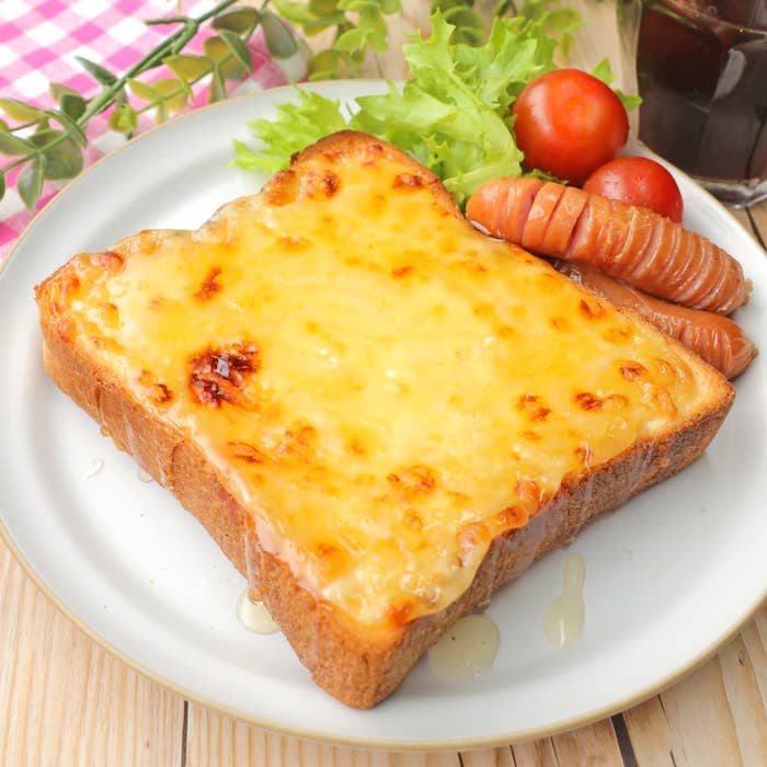 厚切りトーストのチーズ乗せ、ソーセージ、トマト、レタスが添えられた朝食プレート。