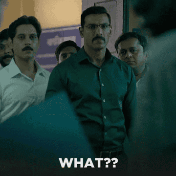 A group of serious-looking men with mustaches stand in a hallway. One man, front and center, appears surprised. Text at the bottom reads "WHAT??"