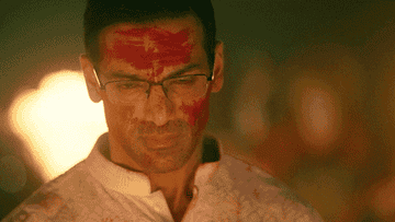 Person with glasses and red tilak on forehead appears contemplative in traditional attire at a festive event