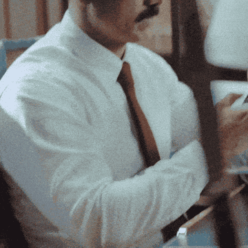 Person in a tie working at a desk, focused on paperwork and writing notes