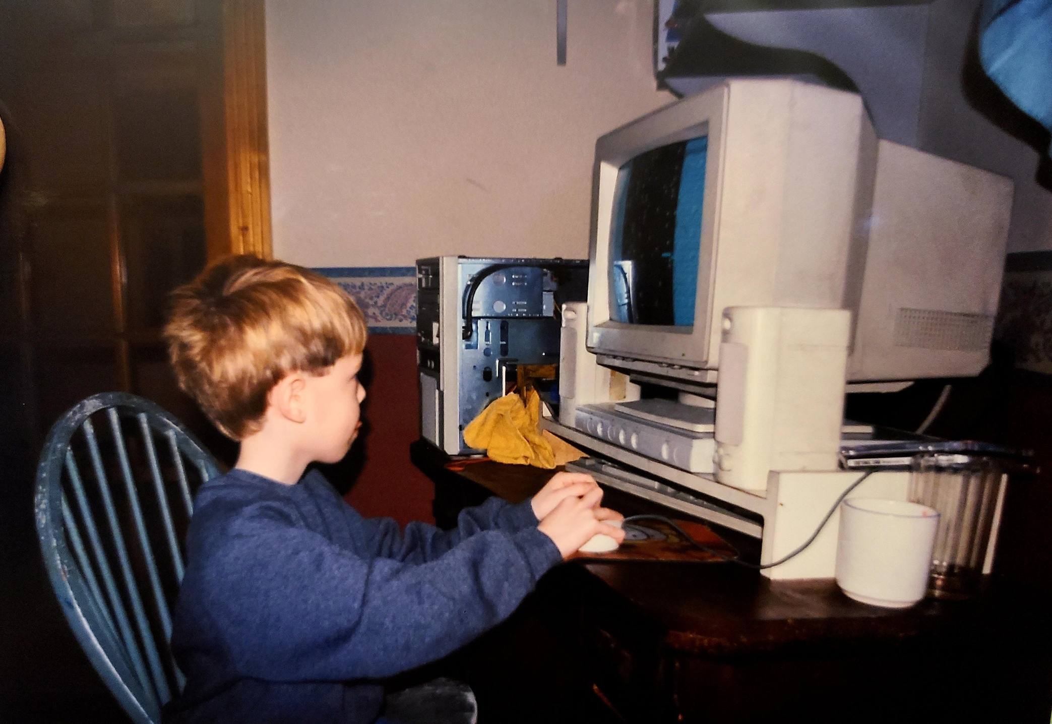 Young child using an old desktop computer with a CRT monitor, seated at a desk, focused on the screen