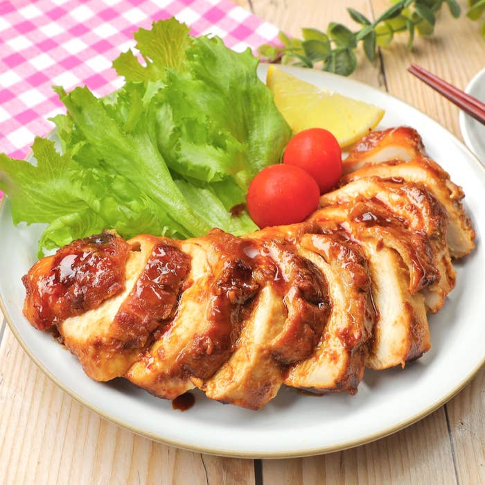 照り焼きソースをかけたグリルチキン、レタス、ミニトマト、レモンが盛られた白い皿。