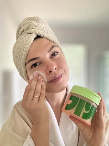 reviewer with a towel wrapped astir their caput applies skincare merchandise utilizing a fabric pad portion holding a jar