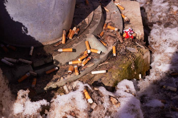 Discarded cigarette butts litter a slushy, snow-covered ground near a concrete structure