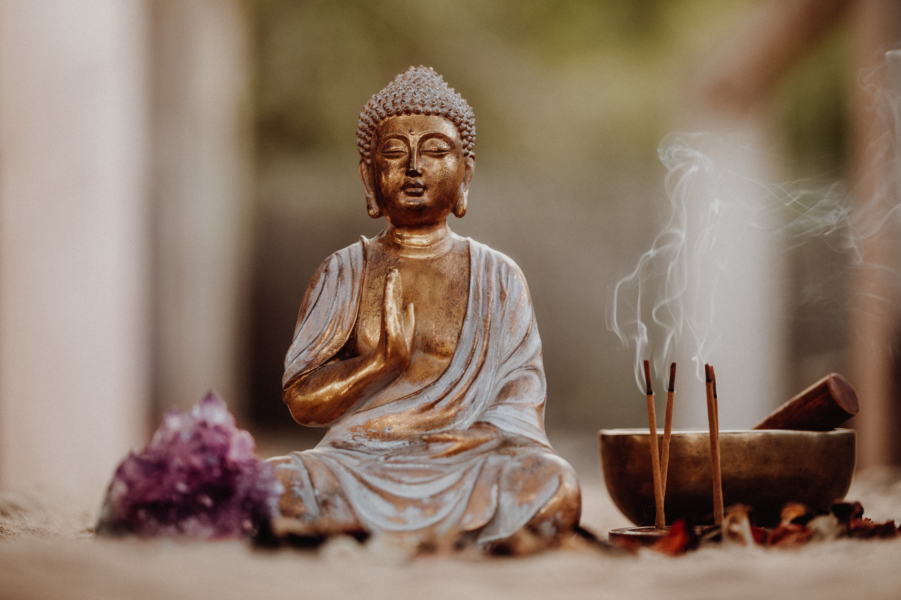 Buddha statue in meditation pose, surrounded by incense sticks emitting smoke, a singing bowl, and amethyst crystals