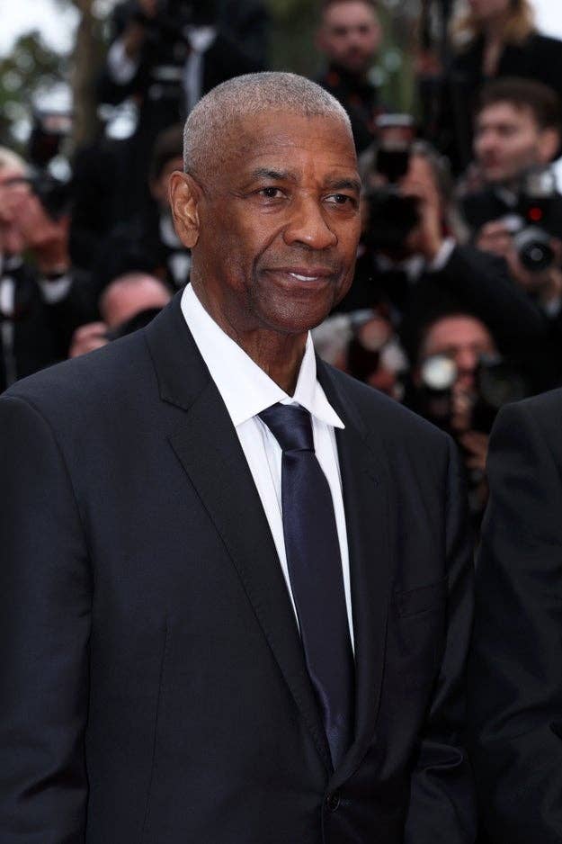 Denzel Washington standing on a Cannes red carpet, surrounded by photographers