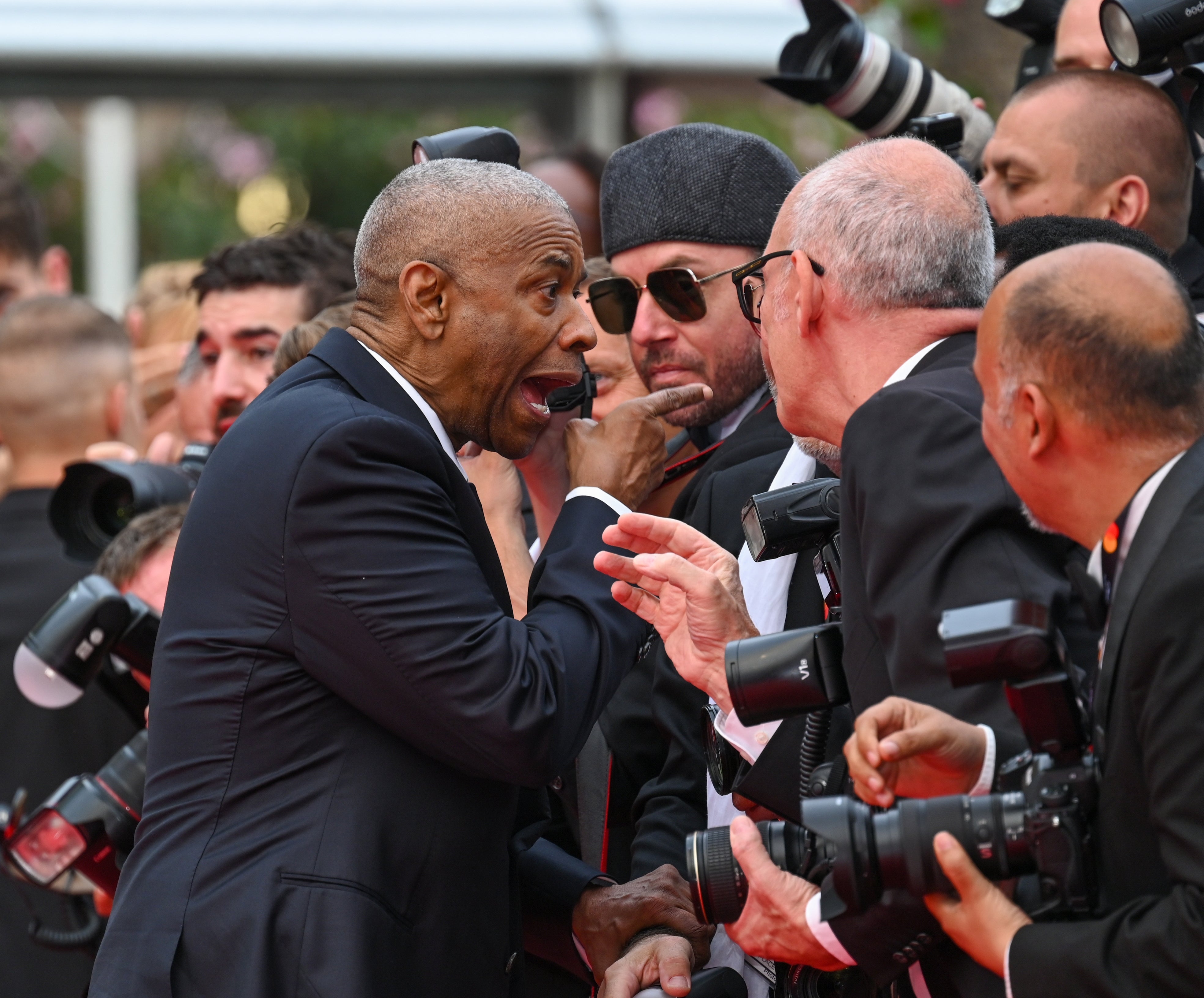 Denzel Washington animatedly shouting at a group of photographers on a crowded red carpet