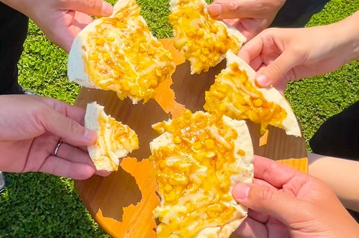 数人が屋外で蜂蜜がかかったパンのピースを手に持っている様子。