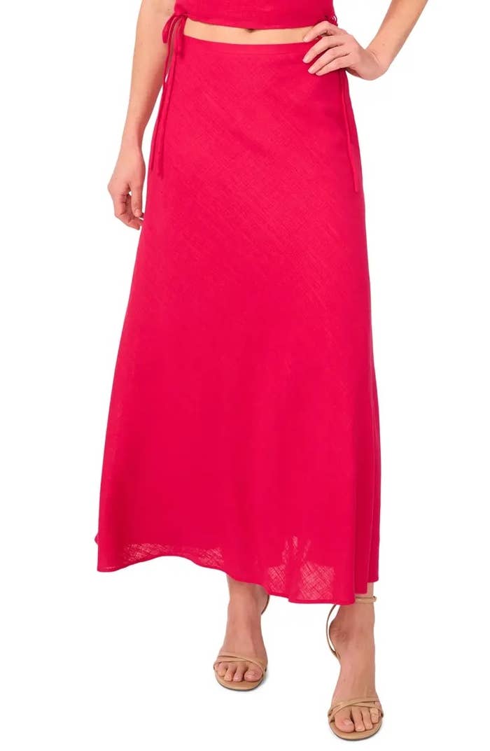 Model wearing a full-length, flowy skirt with necktie  details paired with strappy sandals