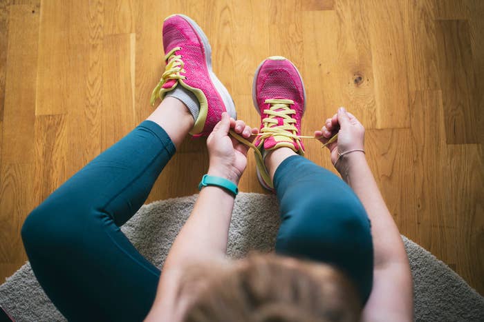 Person in athletic wear tying shoelaces, sitting on a wooden floor