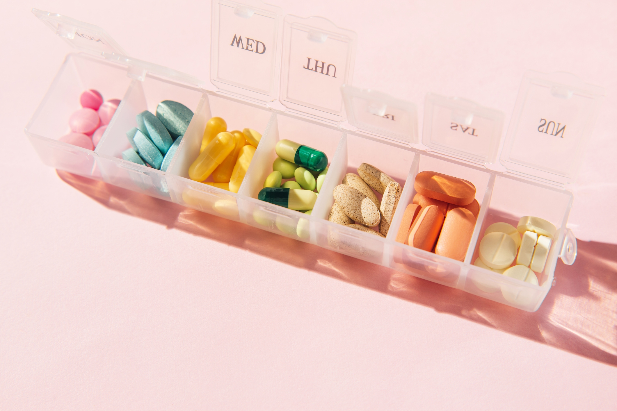 Weekly pill organizer with various pills and supplements sorted by day, shown on a flat surface