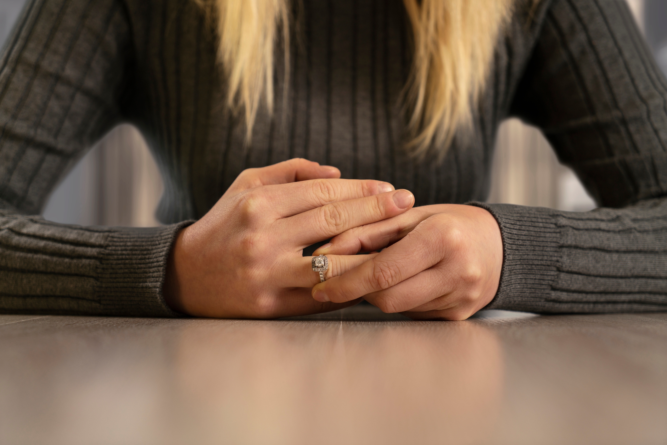 A person wearing a ribbed sweater clasps their hands on a table, showing a ring on their finger