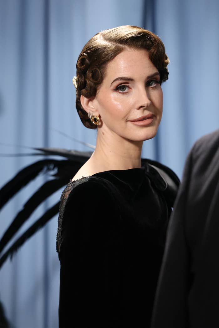 Person with wavy hair in elegant black velvet dress with feather detail, posing on the red carpet