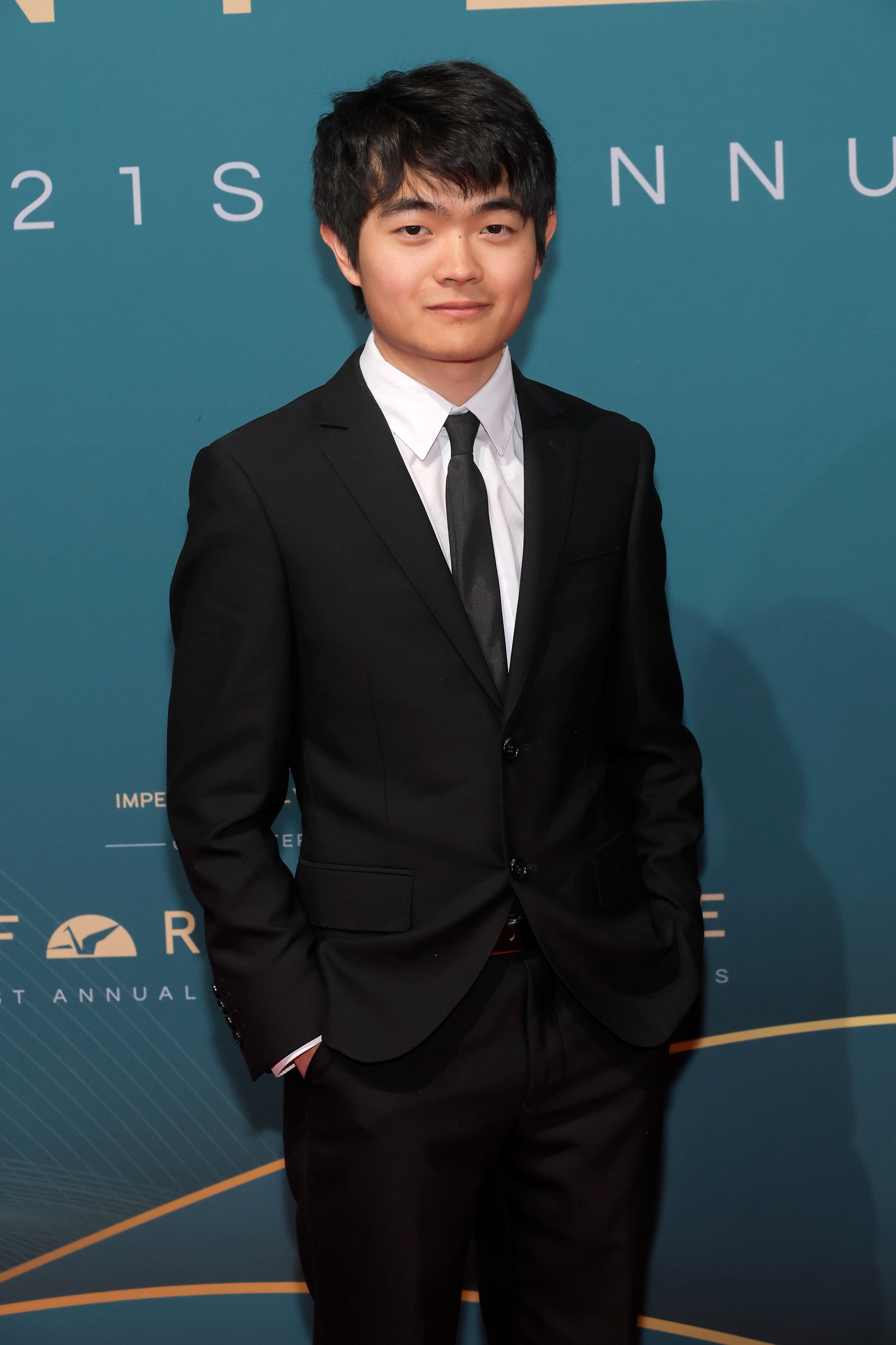 Person in a black suit and tie poses confidently at a formal event