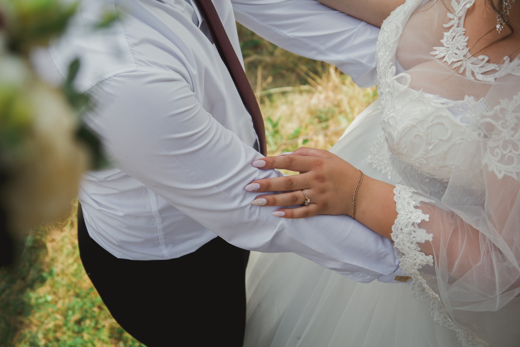 Couple in wedding attire embracing; bride wears a lace gown and groom in a shirt and tie