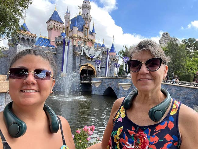 Two radical wearing headphones grin successful beforehand of a castle astatine a taxable park, with a fountain successful view