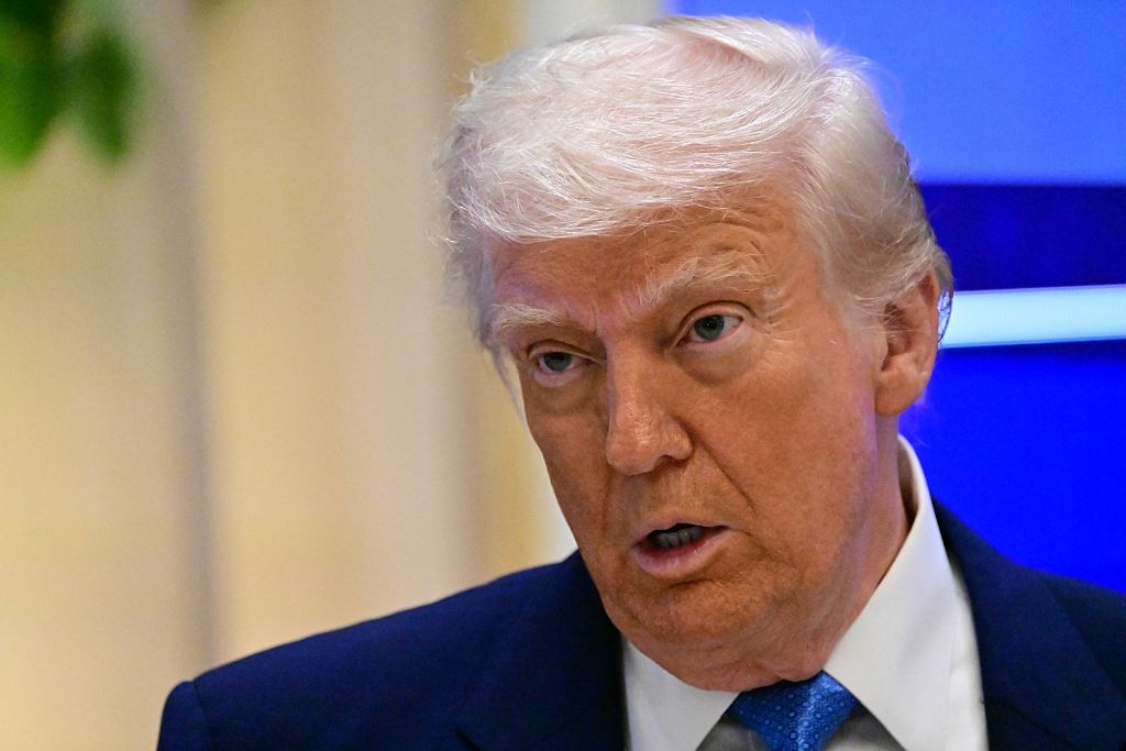 A person in a suit speaks with a serious expression at a public event