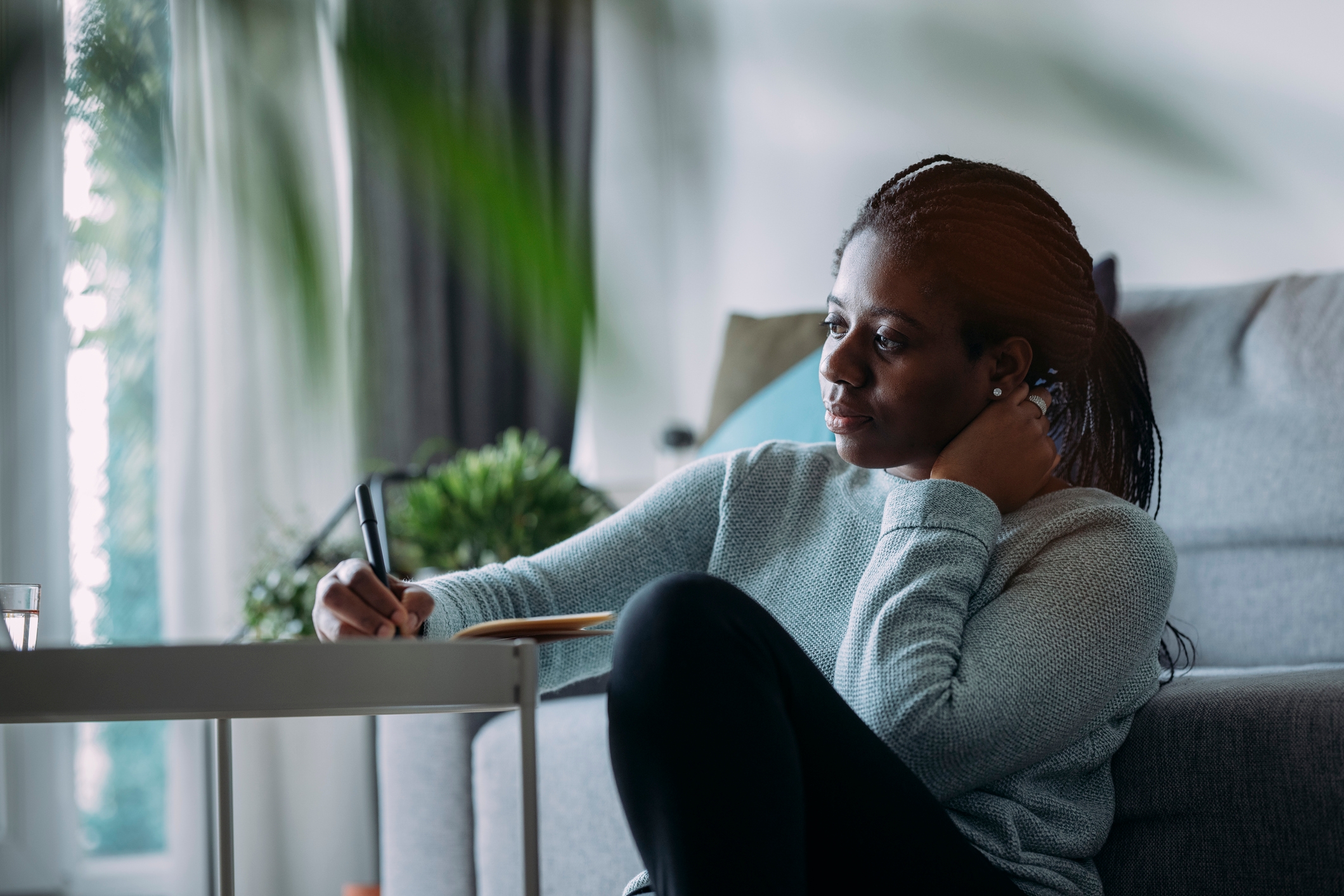 Person sitting on the floor, writing in a notebook, appearing thoughtful in a cozy living room setting