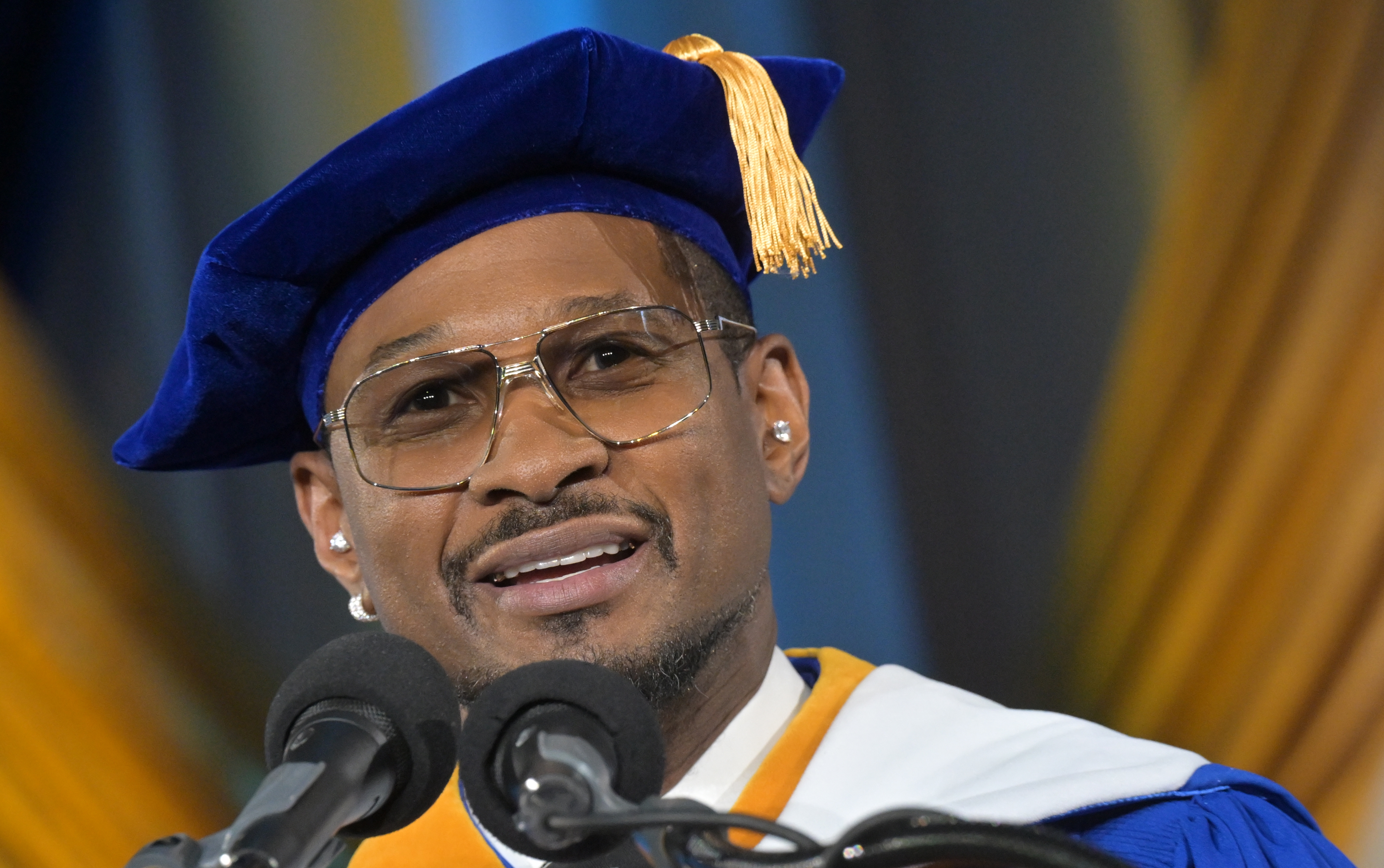 Usher in academic regalia with a cap and tassel speaks at a podium, conveying a sense of achievement and ceremony