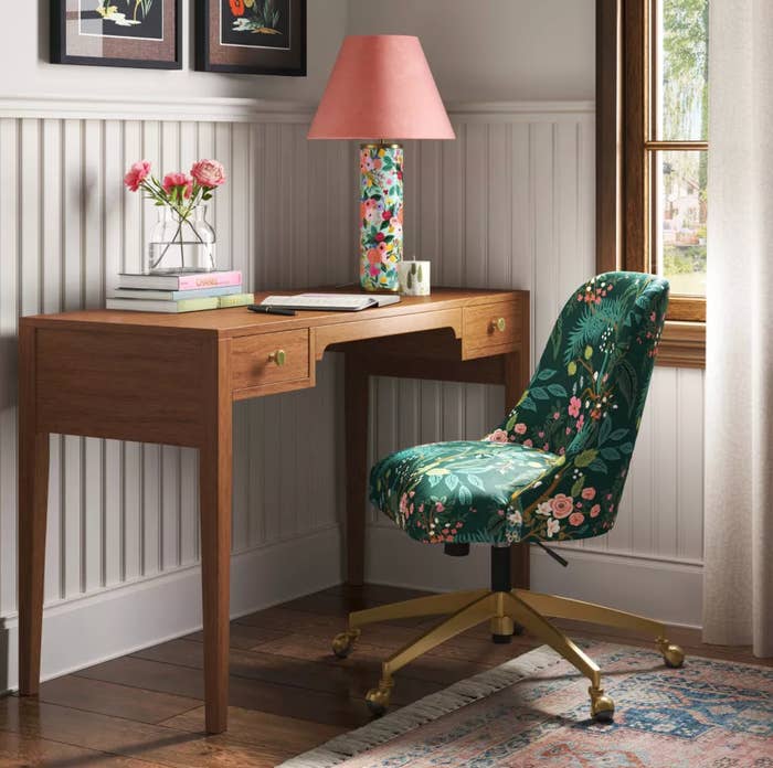 Cozy location bureau with a woody desk, floral chair, and matching lamp; books and flowers adorn the desk, creating a stylish workspace