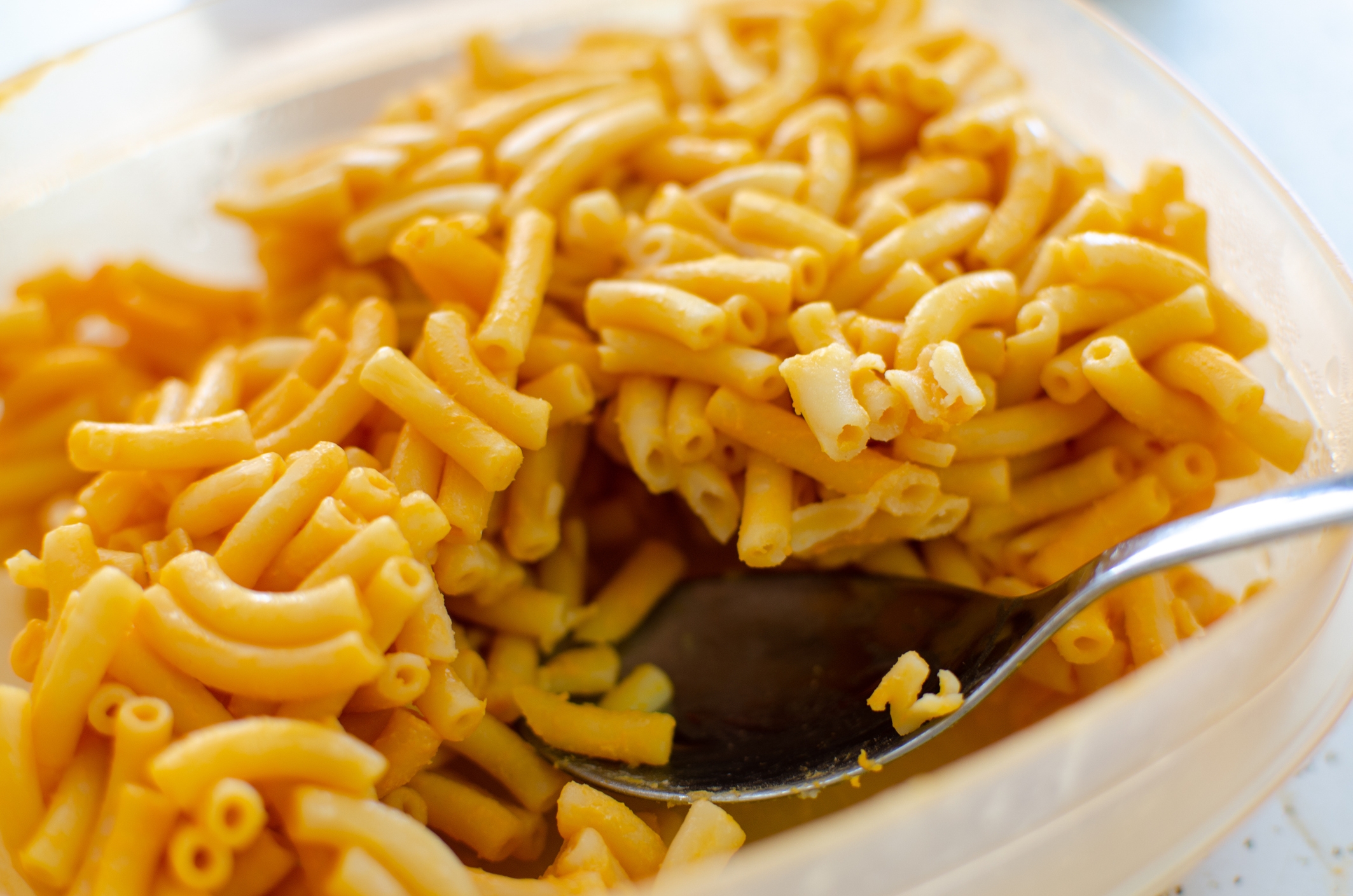 A bowl of macaroni and cheese with a spoon partially immersed in the dish. The pasta is creamy and appears freshly served