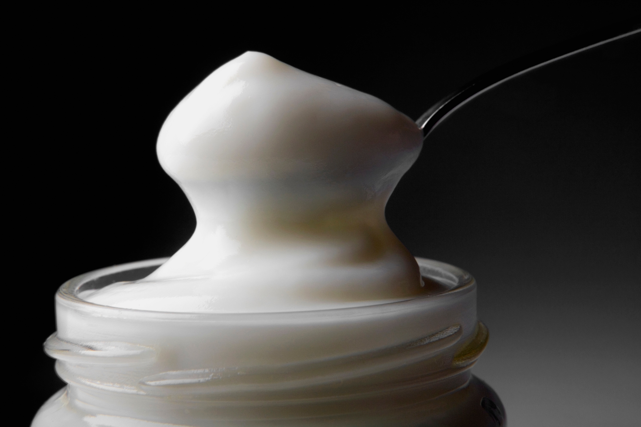 Spoon scooping creamy yogurt from an open jar, set against a dark background