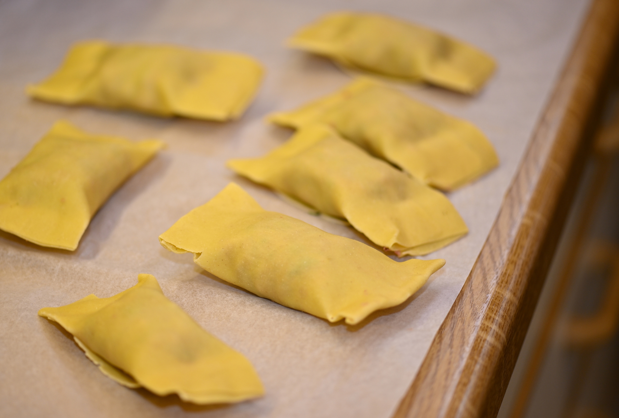 Several rectangular pieces of raw pasta dough filled and folded, placed on a sheet of parchment paper