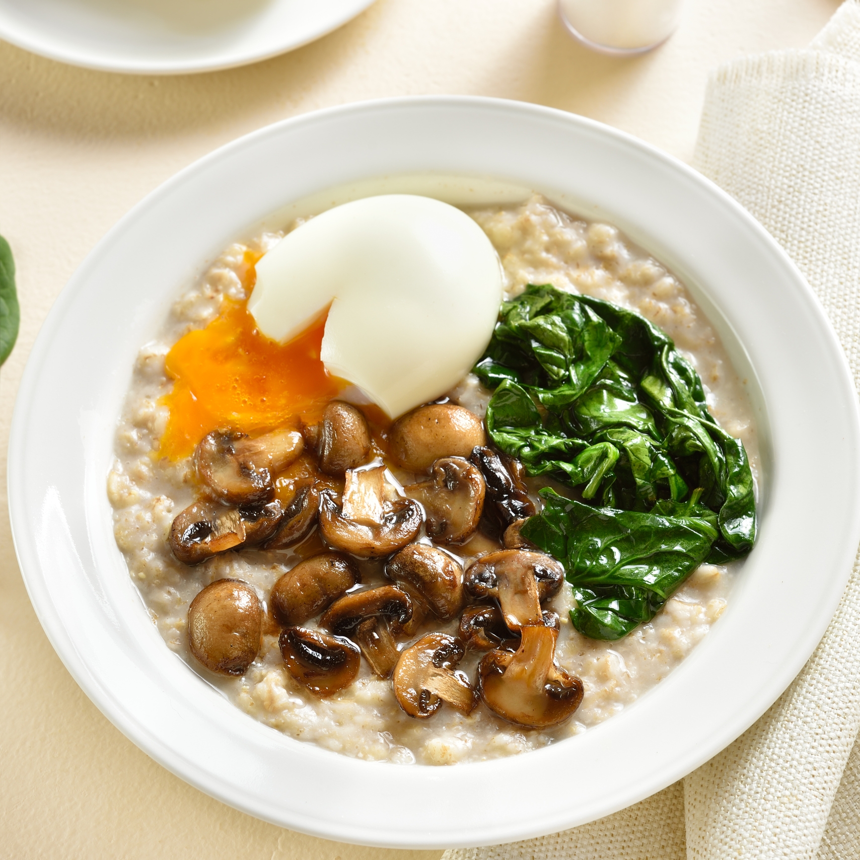 Bowl of oatmeal topped with sautéed mushrooms, spinach, and a poached egg with runny yolk