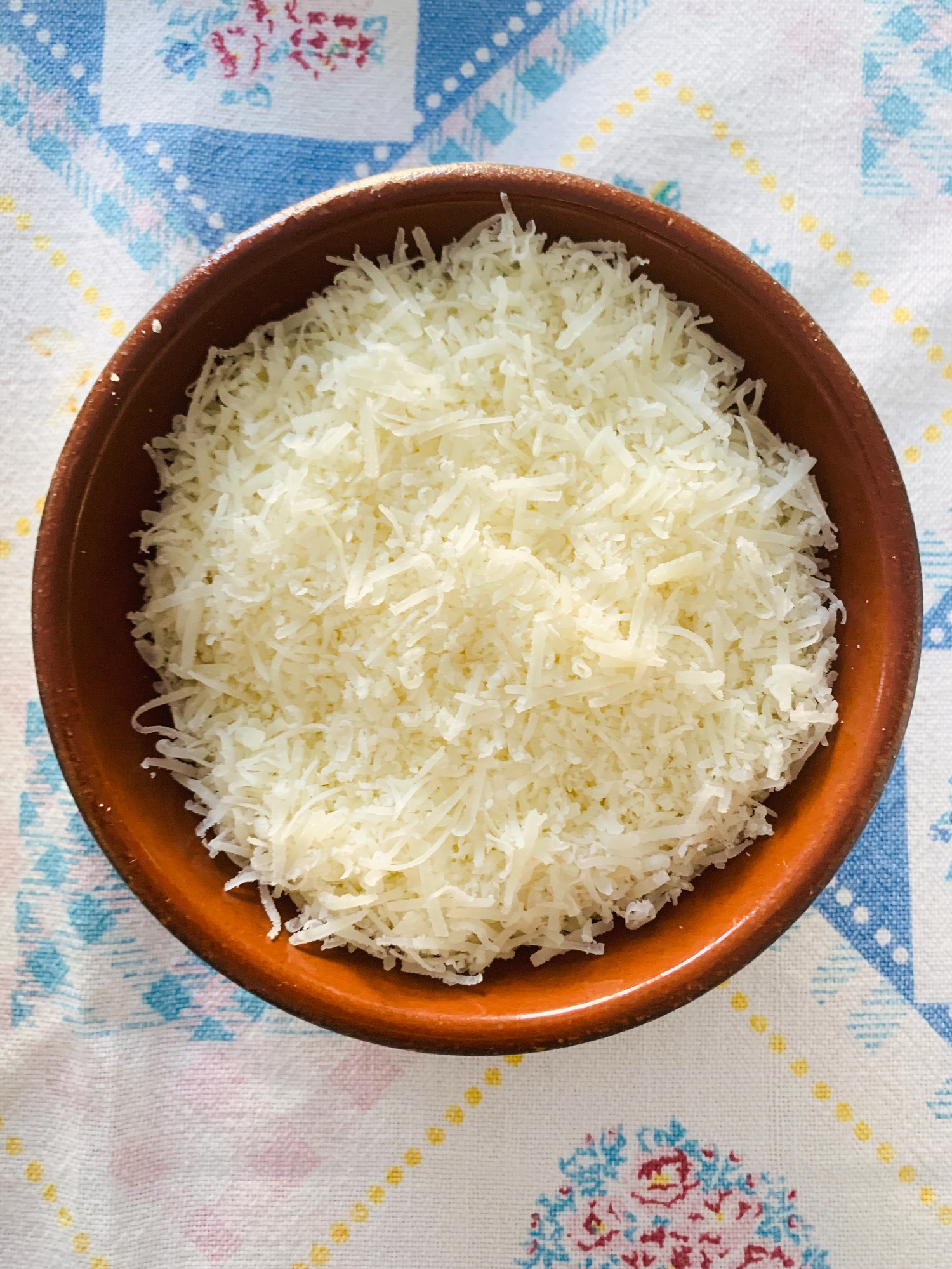 A bowl filled with grated cheese on a patterned tablecloth