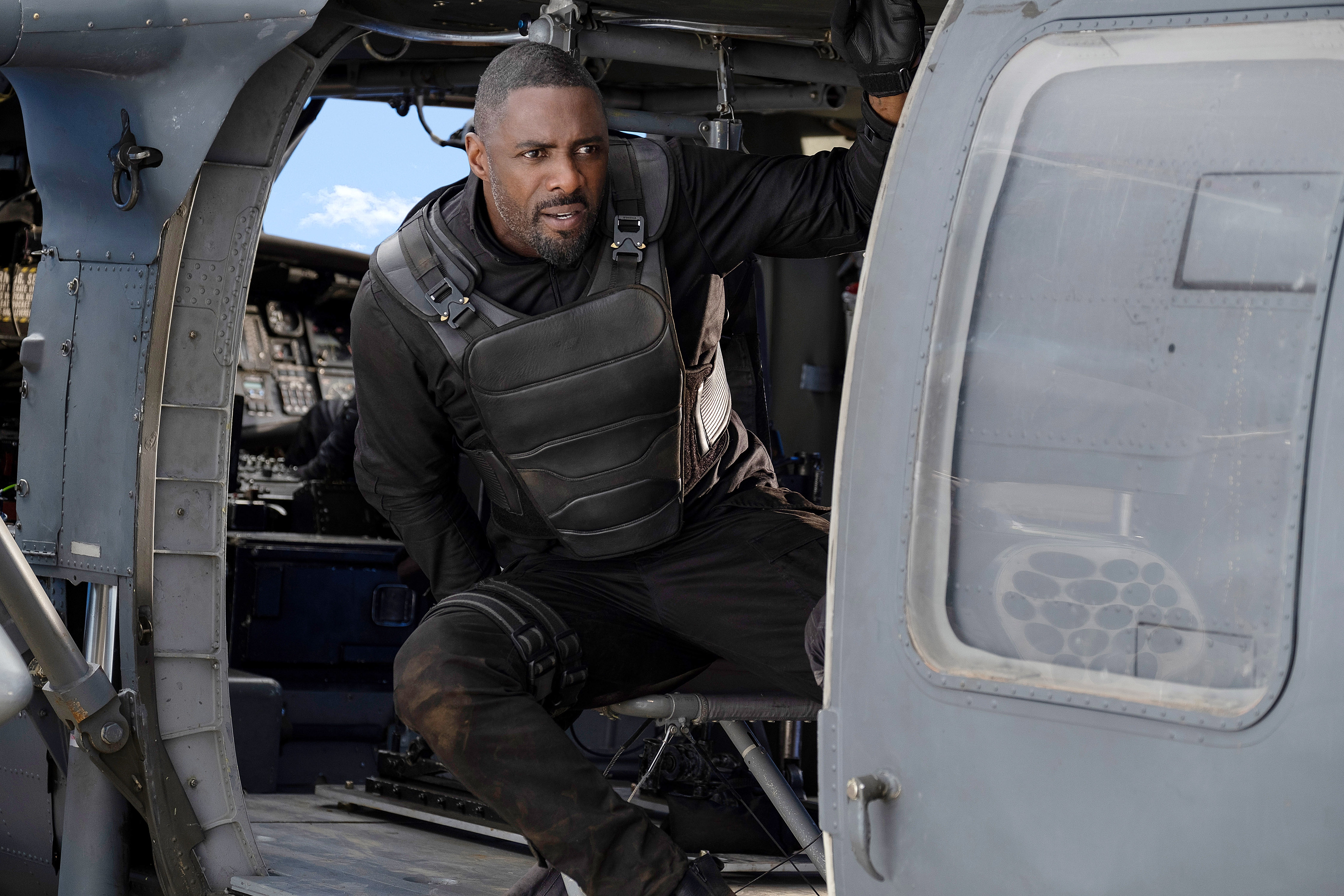 Man in tactical gear in a helicopter, looking focused and ready, seated near an open door