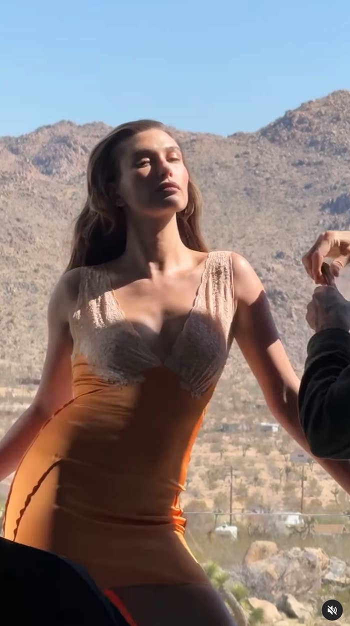 Person posing outdoors successful beforehand of mountains, wearing a fitted, sleeveless formal with lace details, eyes closed, sunlight connected their face