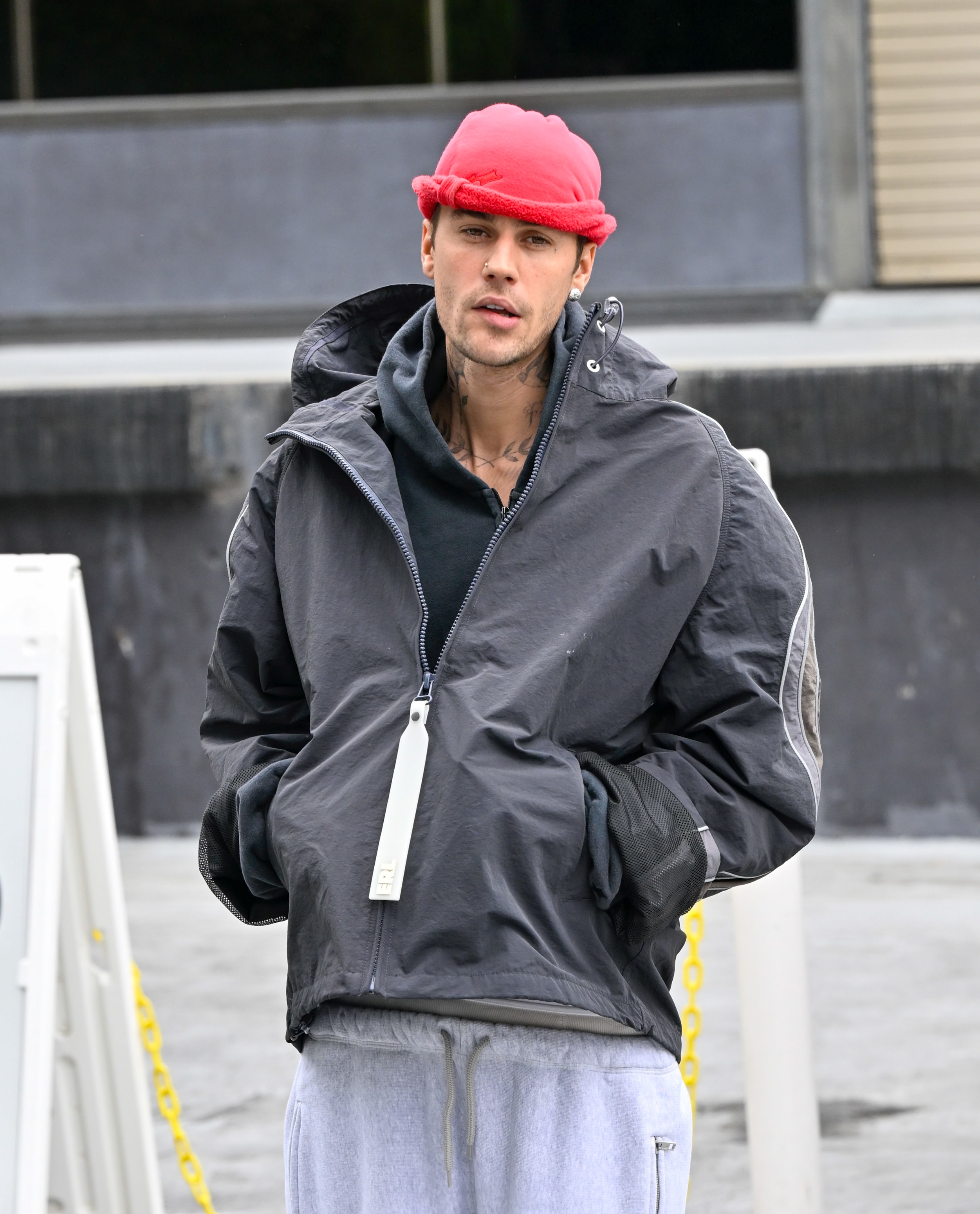 Person in a casual outfit with a red beanie, gray jacket, and sweatpants standing outdoors