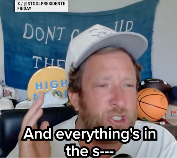 Person wearing a cap gestures while speaking in front of a banner and sports items. Subtitles read, "And everything's in the s—."