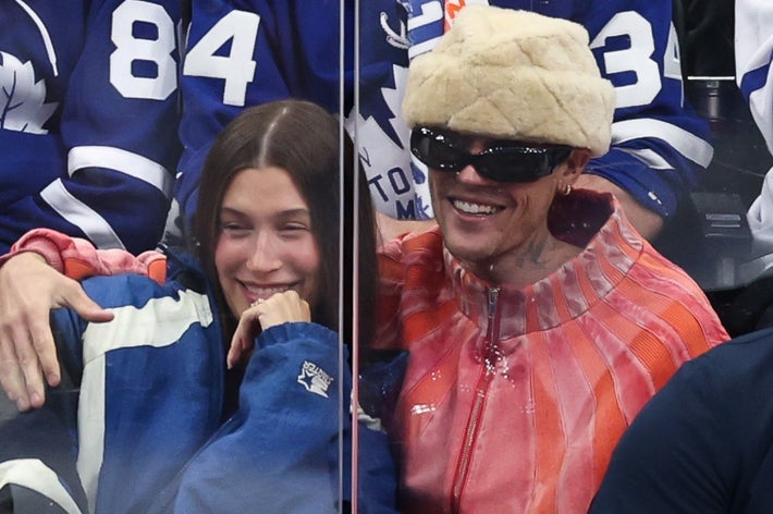 Hockey players on bench during a game; people in suits nearby. Fans in team jerseys watch from behind the glass, showing excitement and engagement