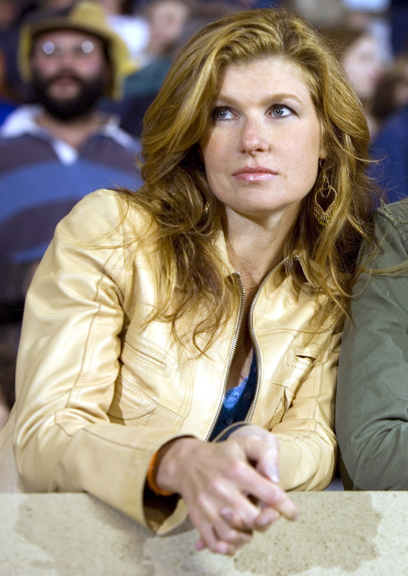 Two women lean on a railing, watching an event. One wears a light jacket, the other a darker one with a pin. They appear focused and engaged