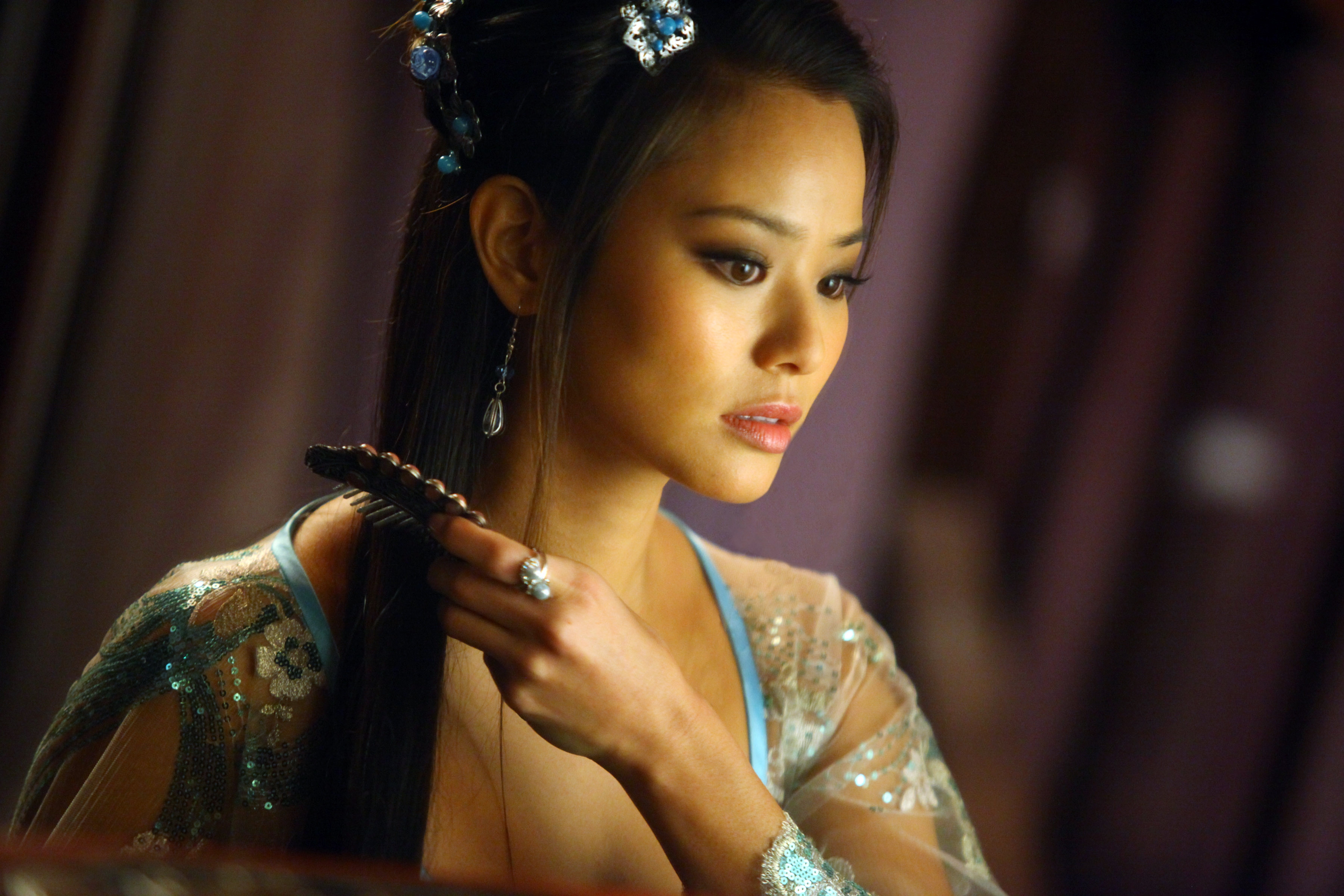 Person wearing a detailed, semi-transparent gown, adorned with floral patterns, is brushing their hair and looking serene