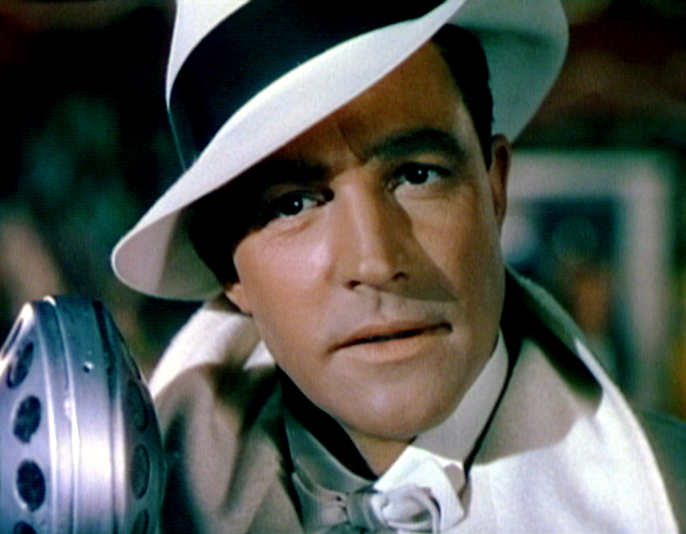 Actor in a classic film scene, wearing a fedora and bow tie, gazes thoughtfully beside an old-style microphone