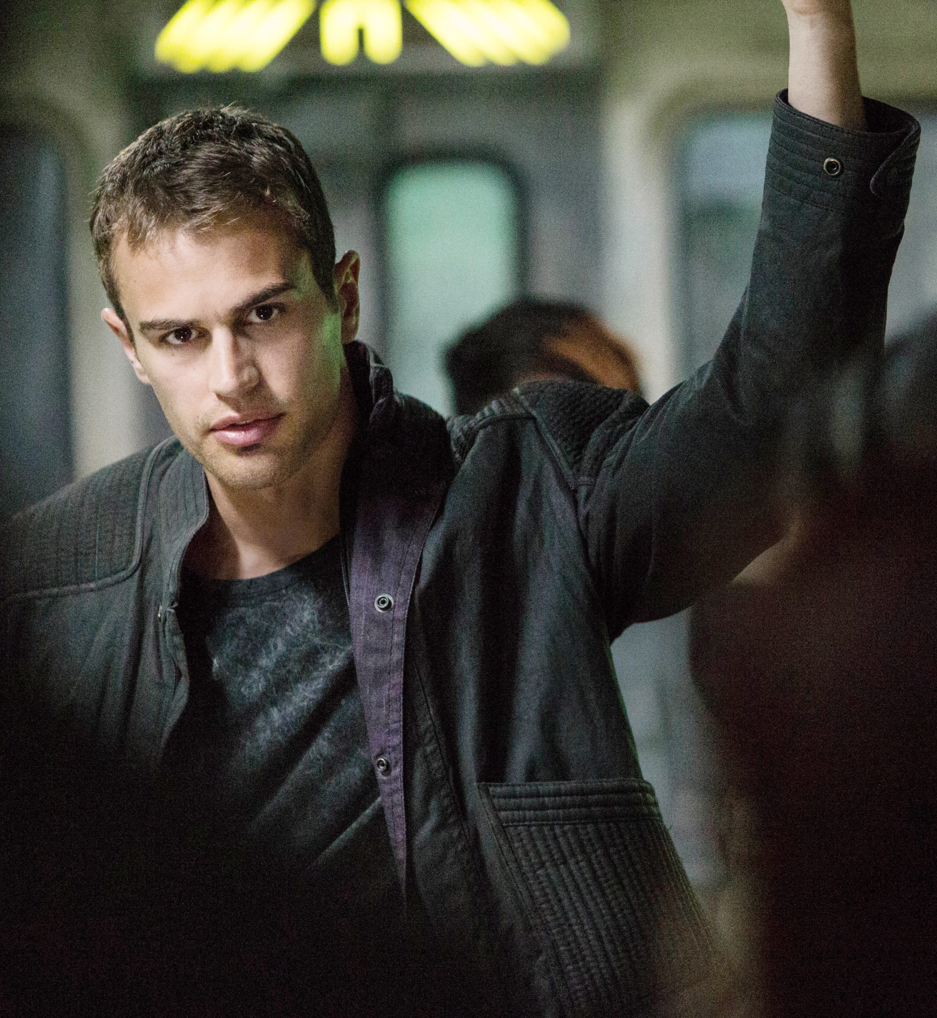 Man wearing a casual black jacket in a focused pose, holding a bar, possibly on public transport