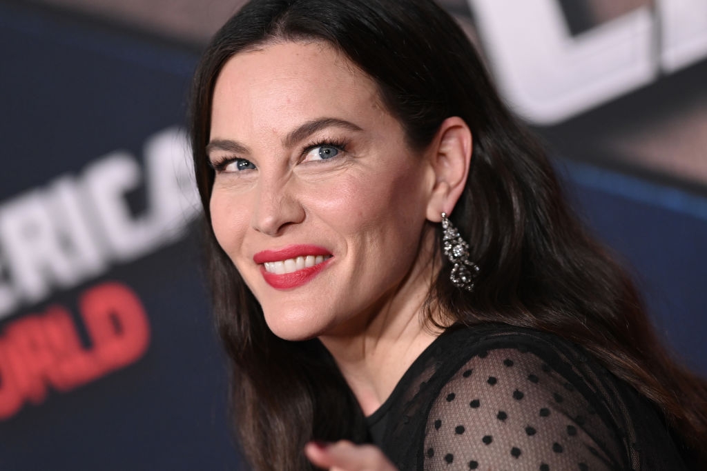 Person smiling on the red carpet, wearing a sheer polka-dot black top with statement earrings