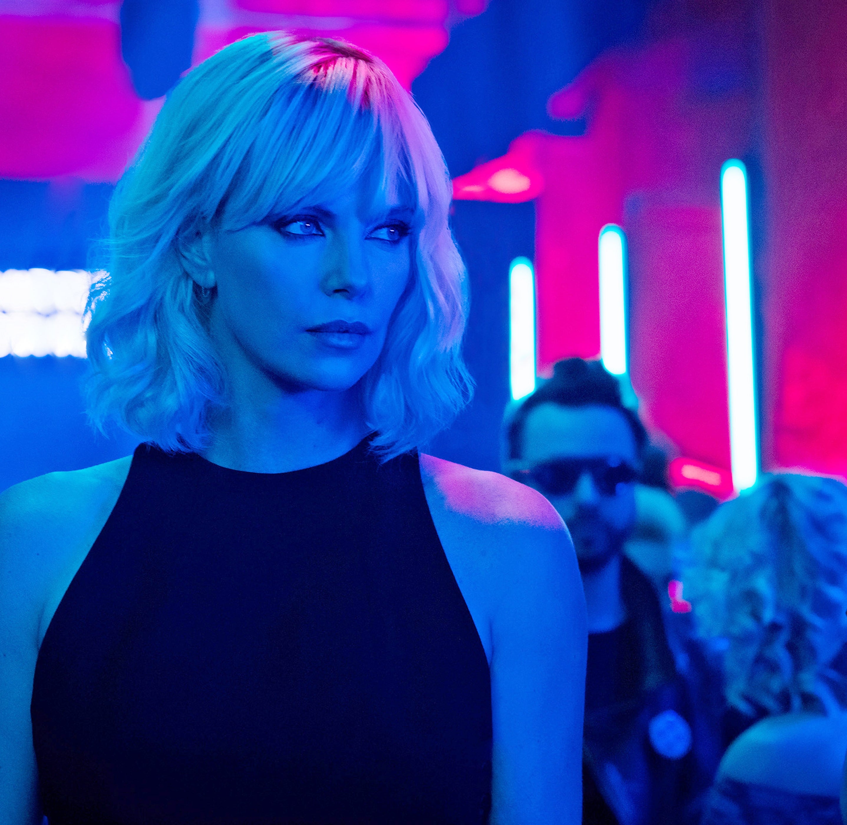 Person in a sleek black outfit at an event with neon lights and attendees in the background